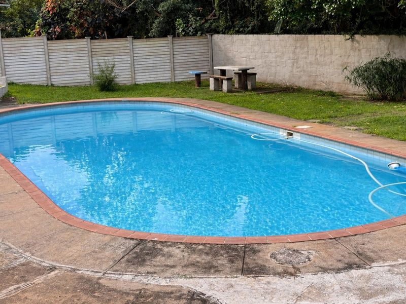 Outdoor swimming pool area featuring a concrete paved surround, lawn, and perimeter boundary walling.