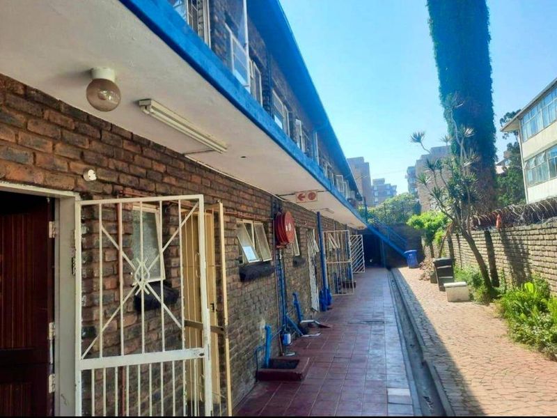 Exterior rear view of an apartment building featuring a tiled walkway, brick facade, and security infrastructure along the perimeter wall.