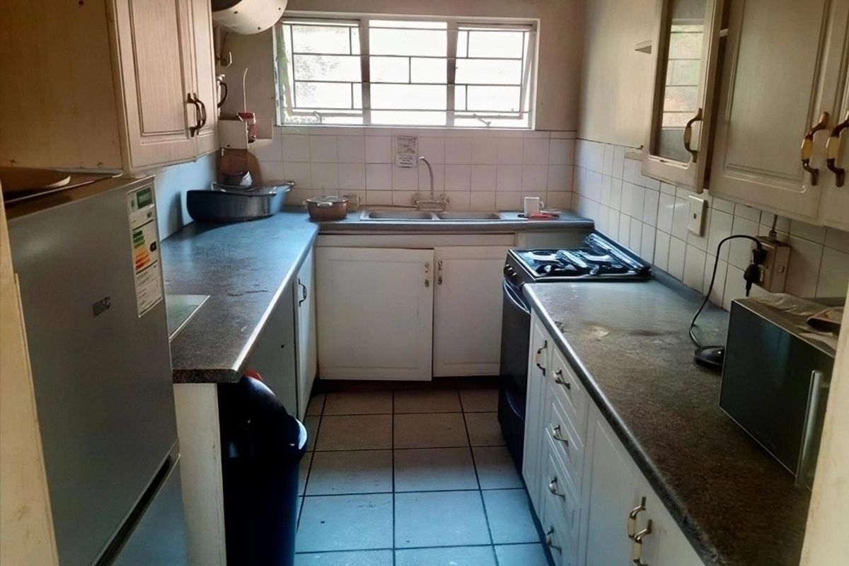 A compact, dated kitchen featuring laminate countertops, tiled backsplash, double basin sink, and built-in cabinetry with tiled flooring.