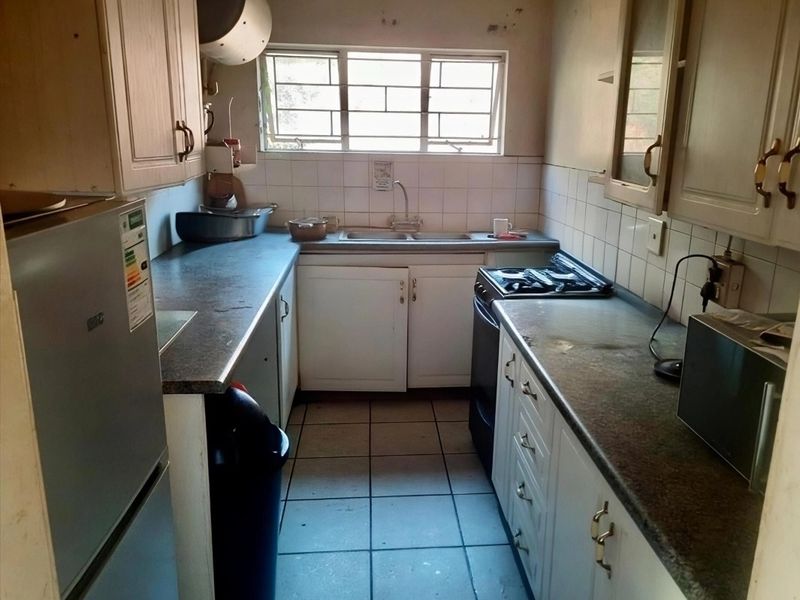 A compact, dated kitchen featuring laminate countertops, tiled backsplash, double basin sink, and built-in cabinetry with tiled flooring.