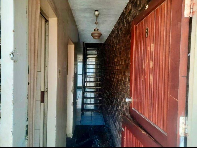 A narrow hallway featuring an exposed brick wall, tiled flooring, and a staircase leading to an upper level.