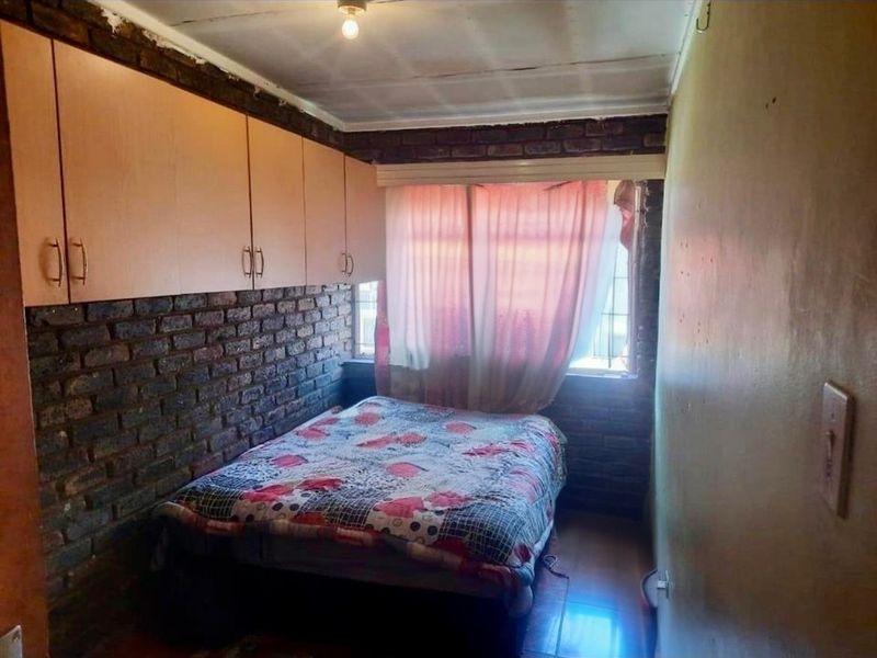 A bedroom featuring exposed brick walls, built-in cupboards, and security bars on the window. The room requires cosmetic updates to improve its overall condition.