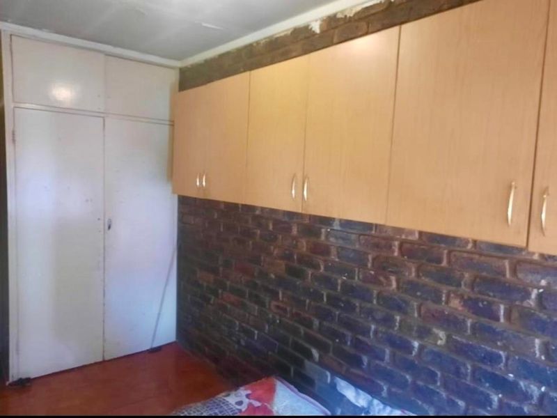 Bedroom featuring exposed brick walls, built-in wooden cabinetry, and laminate flooring. The space requires minor ceiling repairs and cosmetic updates.