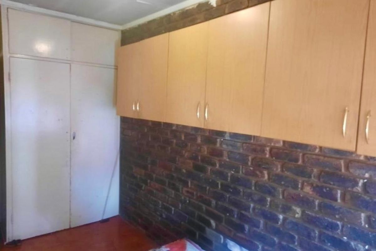 Bedroom featuring exposed brick walls, built-in wooden cabinetry, and laminate flooring. The space requires minor ceiling repairs and cosmetic updates.