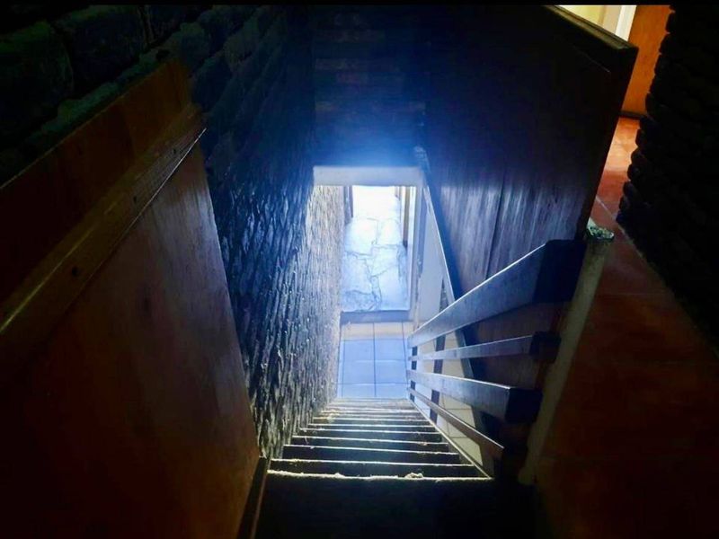 A narrow staircase with exposed brick walls and a wooden handrail leading down to a tiled landing area.