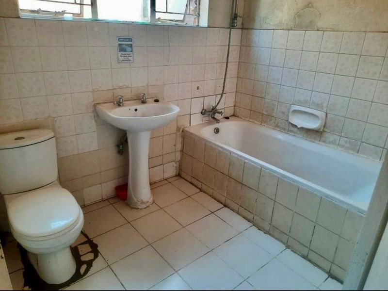 A dated bathroom featuring a pedestal basin, bathtub, and toilet, requiring significant renovation and cosmetic updates to improve its condition and functionality.