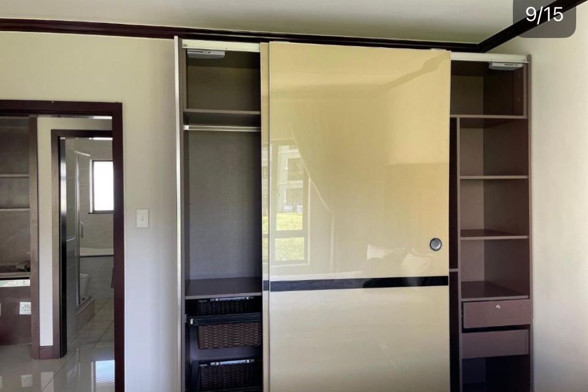 Bedroom featuring a modern built-in wardrobe with sliding doors, integrated shelving, and drawers, with an adjacent view into the en-suite bathroom.