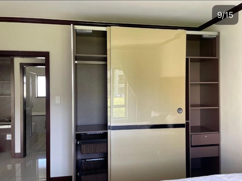 Bedroom featuring a modern built-in wardrobe with sliding doors, integrated shelving, and drawers, with an adjacent view into the en-suite bathroom.