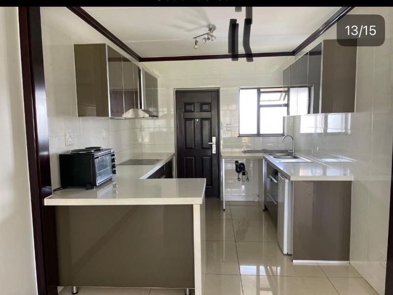 A modern kitchen featuring glossy cabinetry, stone countertops, and tiled finishes. The space is clean and functional, ready for final touches.
