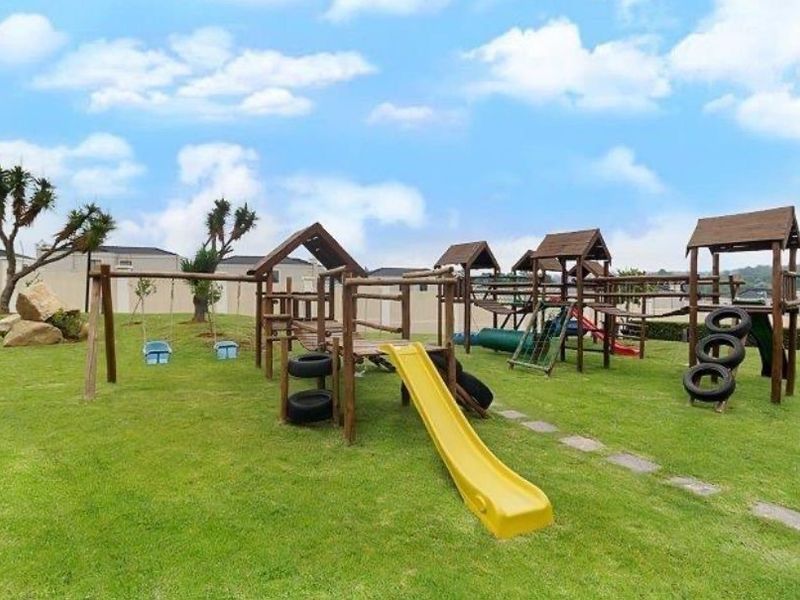 A well-maintained communal garden area featuring a large wooden playground structure with slides and swings set on a grassy lawn.