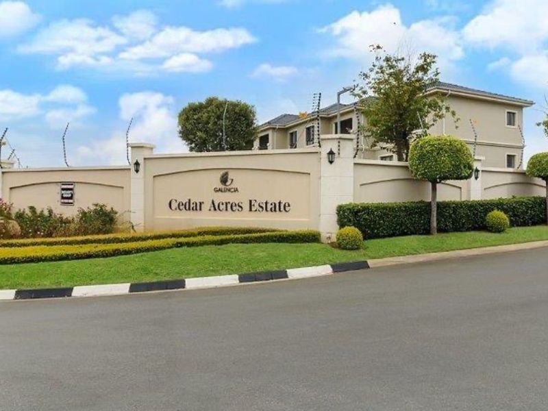 The entrance facade of Cedar Acres Estate featuring a well-maintained perimeter wall, electric fencing, and manicured landscaping.