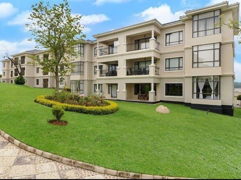 A view of the rear apartment building facade featuring multiple balconies, large windows, and a well-maintained landscaped garden area.