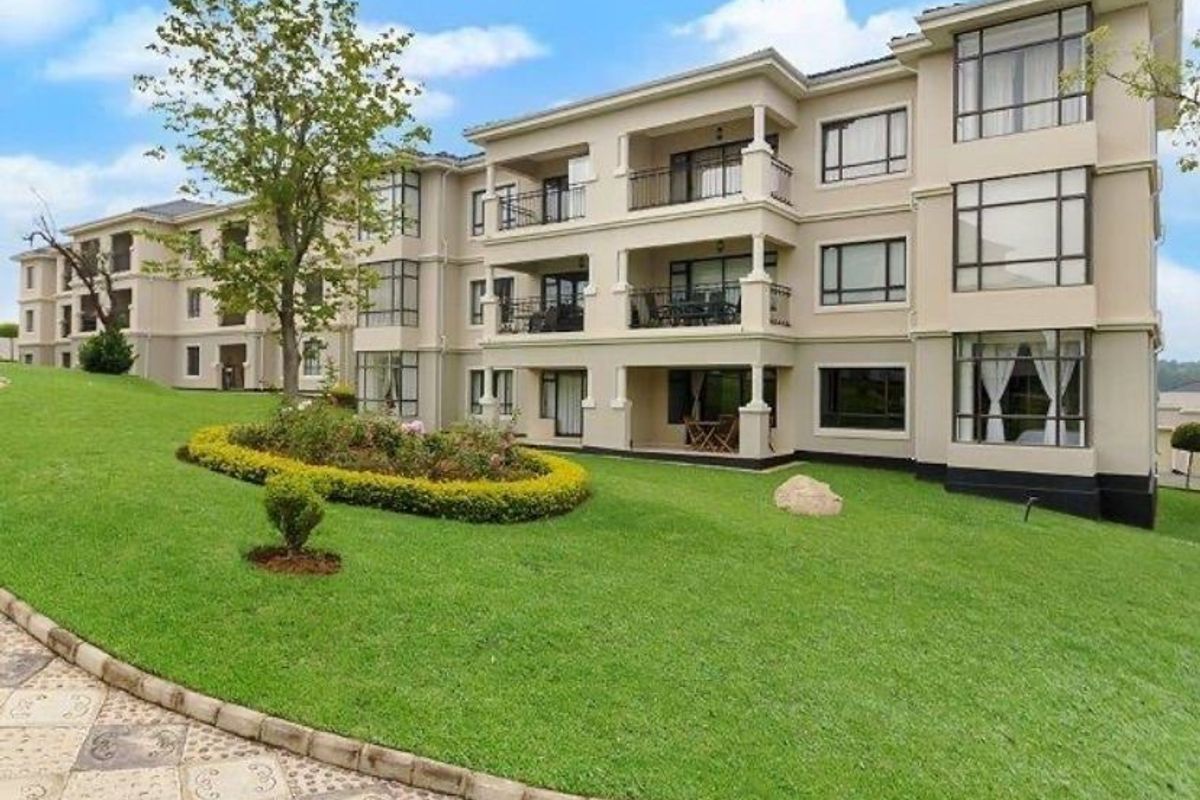 A view of the rear apartment building facade featuring multiple balconies, large windows, and a well-maintained landscaped garden area.