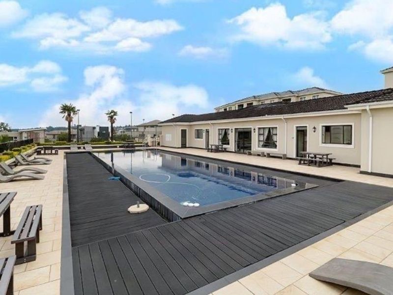 A well-maintained communal swimming pool area featuring composite decking, tiled patio surrounds, and direct access to the apartment building exterior.