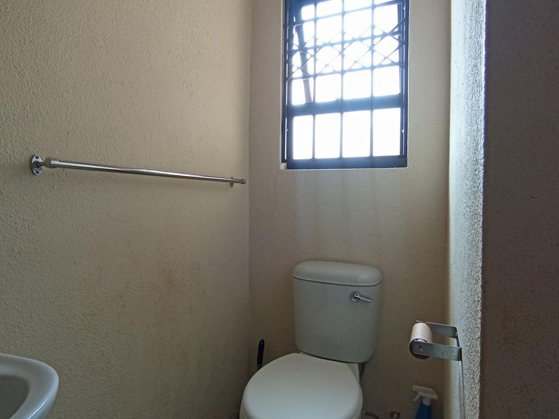 A compact bathroom featuring a standard toilet, washbasin, and a window with security bars. The space requires cosmetic updates to the wall finishes.