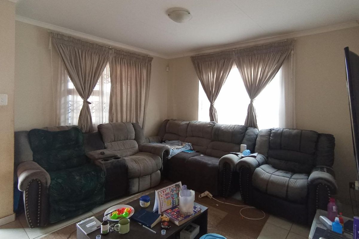 A comfortable living room featuring tiled flooring, neutral wall finishes, and dual windows with installed curtain rails.