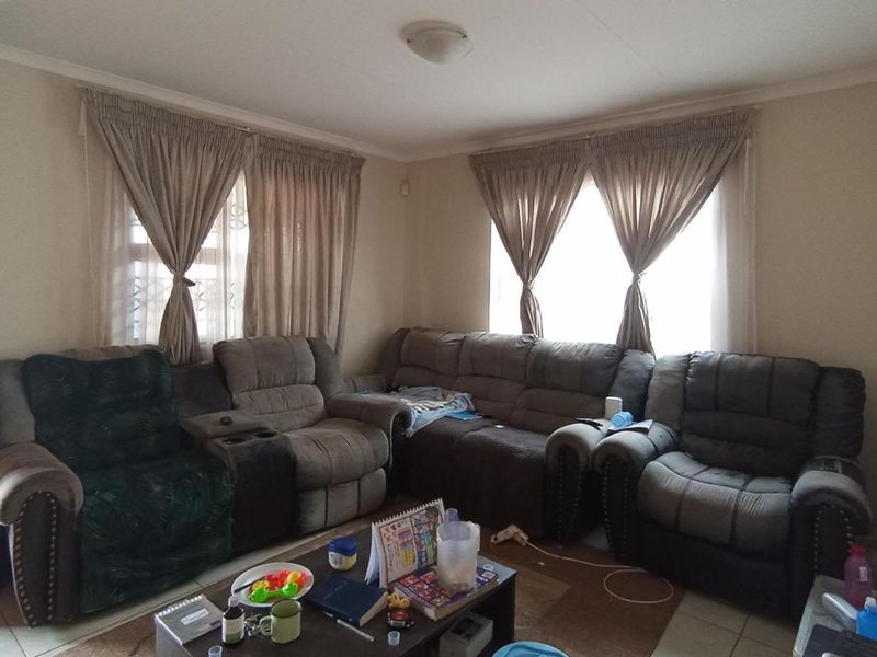 A comfortable living room featuring tiled flooring, neutral wall finishes, and dual windows with installed curtain rails.