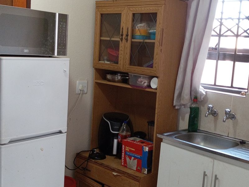 A functional kitchen area featuring a stainless steel sink, built-in cabinetry, and tiled flooring, currently showing signs of age and wear.