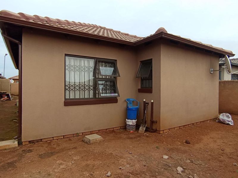 Rear view of the property featuring plastered walls, tiled roofing, and security-fitted windows, set against an unlandscaped yard area.