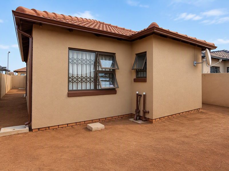 A view of the rear exterior of the house featuring terracotta roof tiles, security bars on windows, and a clean, low-maintenance yard area.