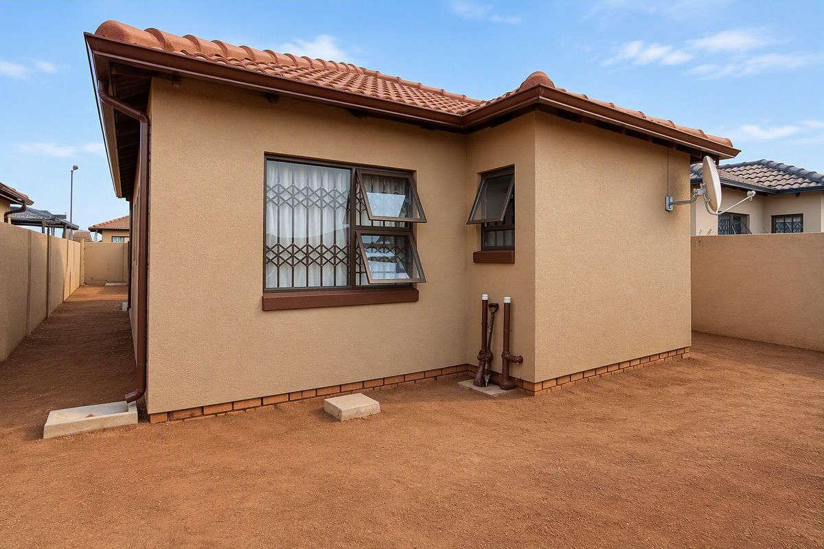 A view of the rear exterior of the house featuring terracotta roof tiles, security bars on windows, and a clean, low-maintenance yard area.