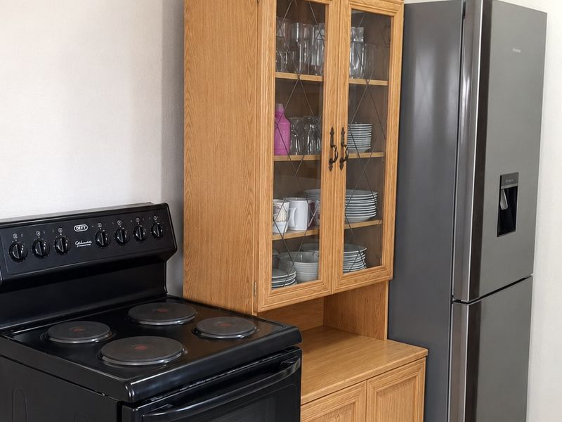 A functional kitchen area featuring a black electric stove, wooden cabinetry with glass display doors, and modern tiled flooring.