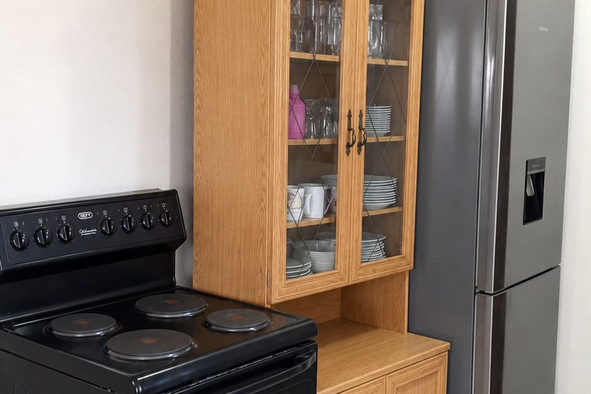 A functional kitchen area featuring a black electric stove, wooden cabinetry with glass display doors, and modern tiled flooring.