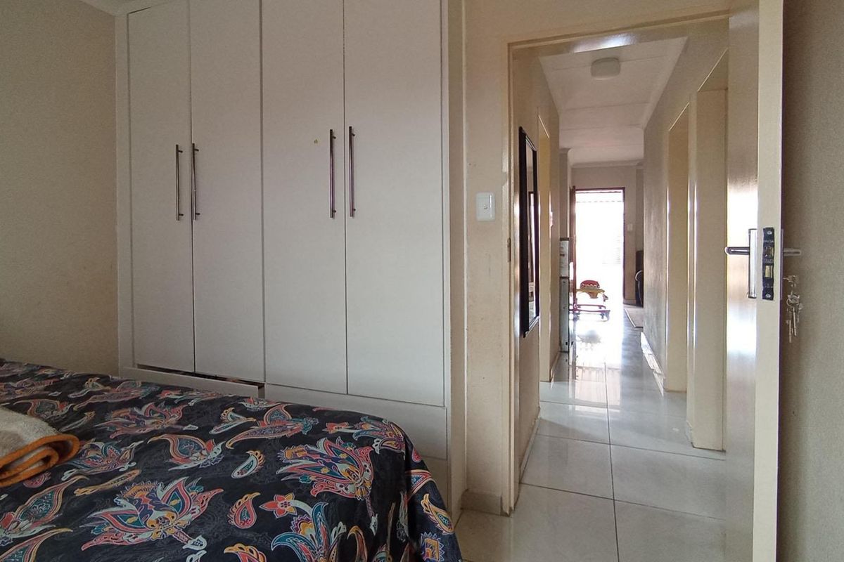 A bedroom featuring built-in cupboards and tiled flooring, with a direct view into the adjacent hallway.
