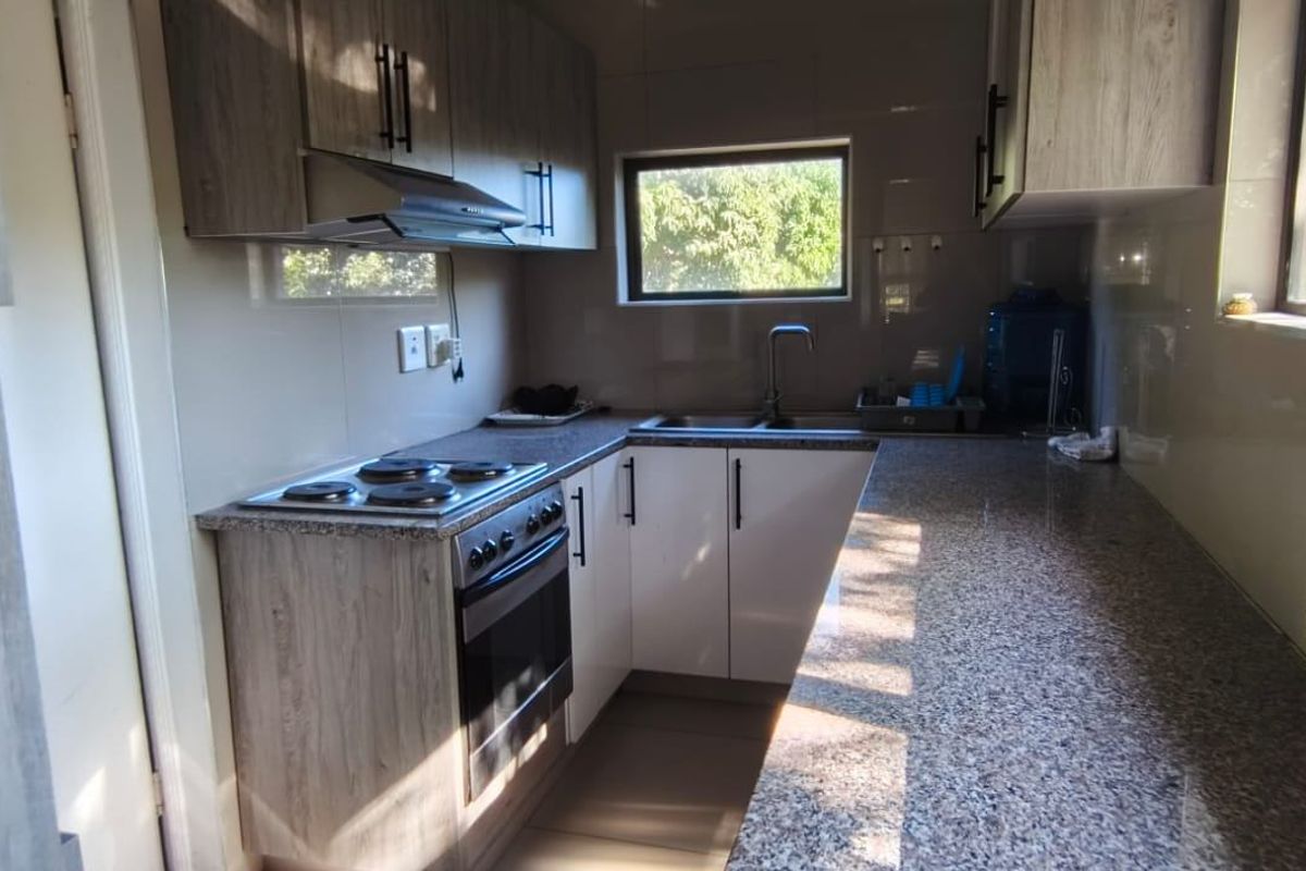 Modern kitchen featuring granite countertops, built-in oven with hob, extractor fan, and ample cabinetry, offering a functional and well-maintained cooking space.