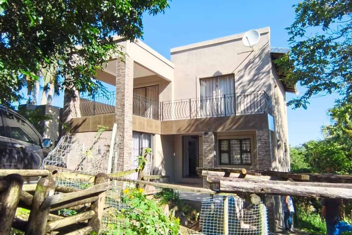 Rear elevation of a two-story house featuring a balcony with wrought iron railings, stone cladding accents, and surrounding garden space.