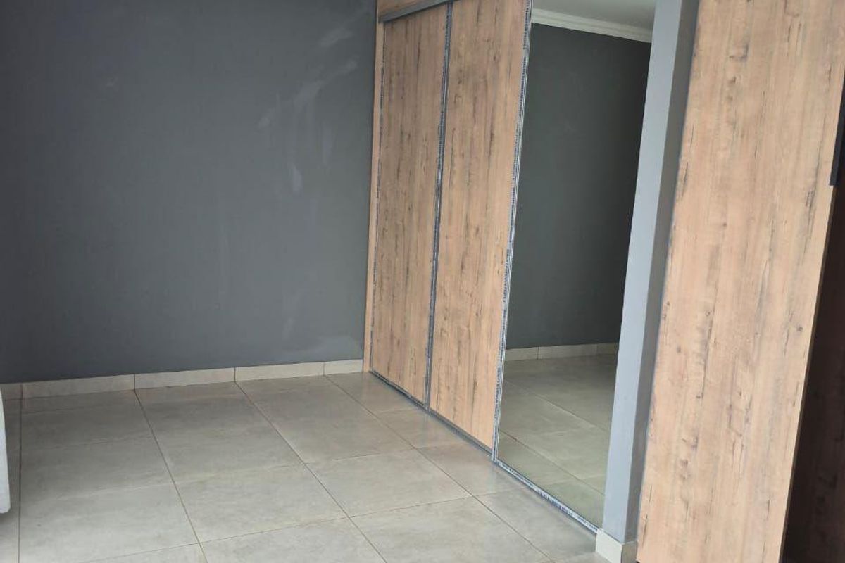 An empty bedroom featuring tiled flooring and a large built-in wardrobe with mirrored sliding doors and wood-grain finish.