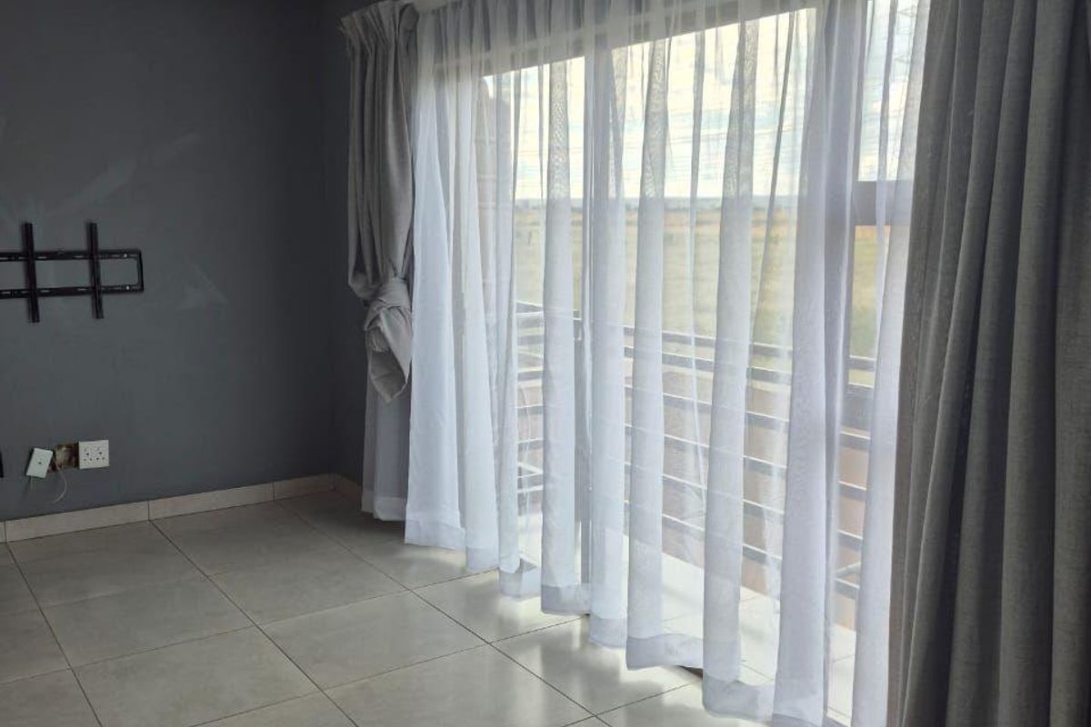 An empty living room featuring large sliding glass doors, neutral tiled flooring, and grey painted walls with a wall-mounted television bracket.