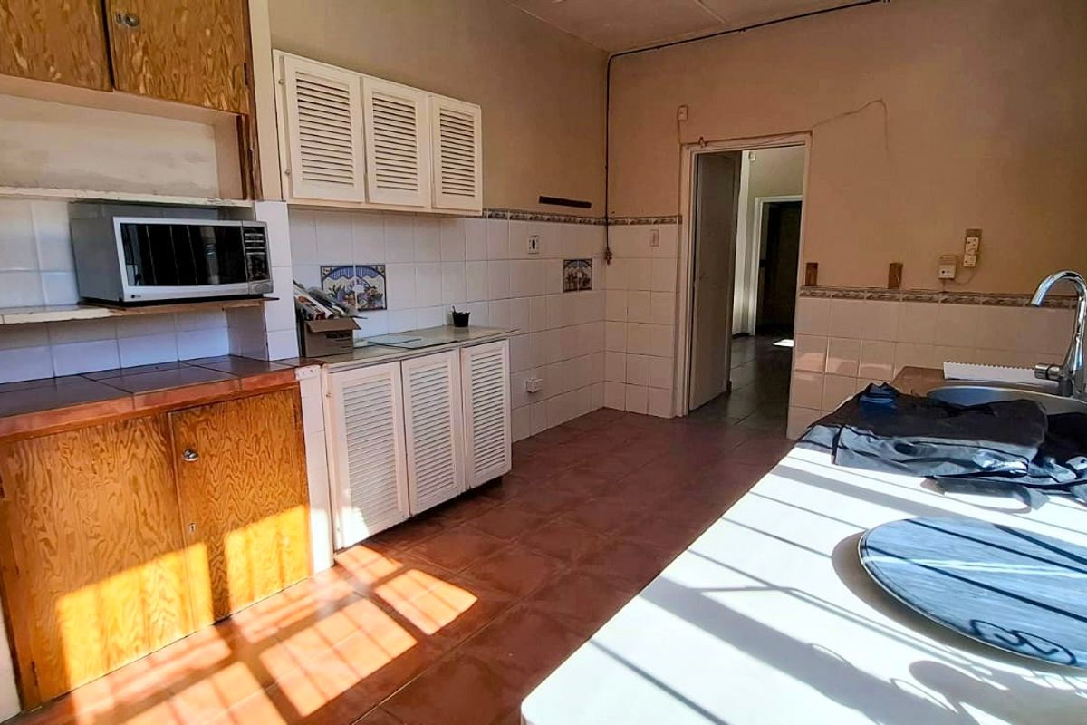 A dated kitchen featuring original wooden cabinetry, tiled countertops, and tiled flooring, requiring modernization to improve functionality and aesthetic appeal.