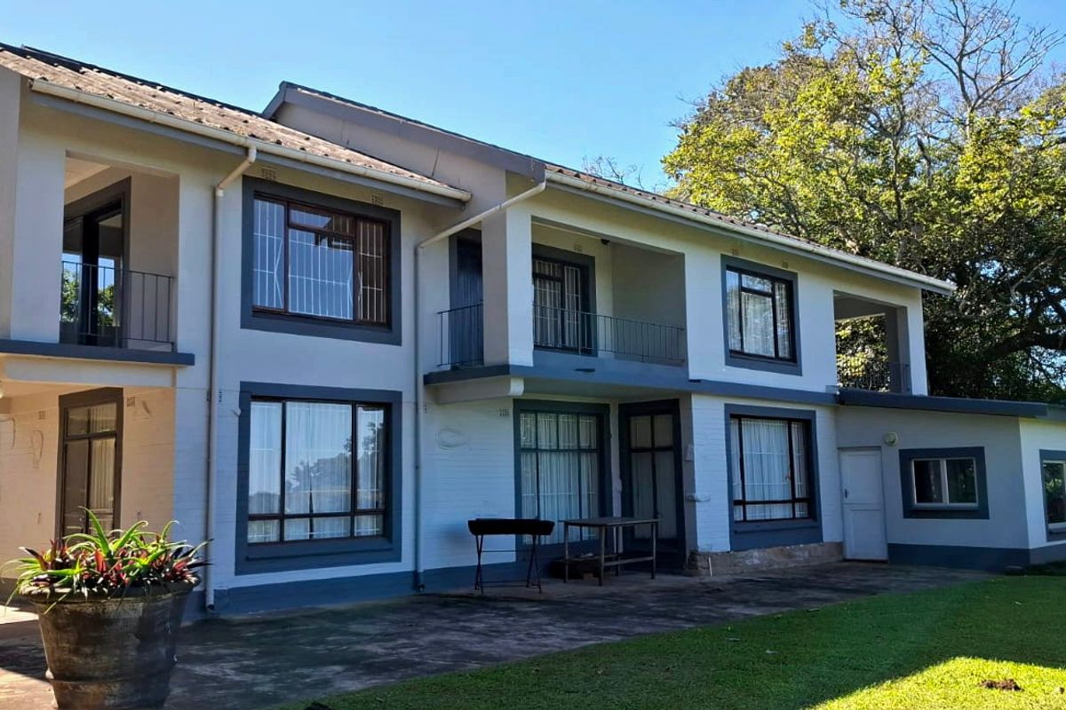 Rear view of a two-story farm residence featuring a concrete patio, upper-level balconies, and well-maintained exterior finishes set against a lush garden.