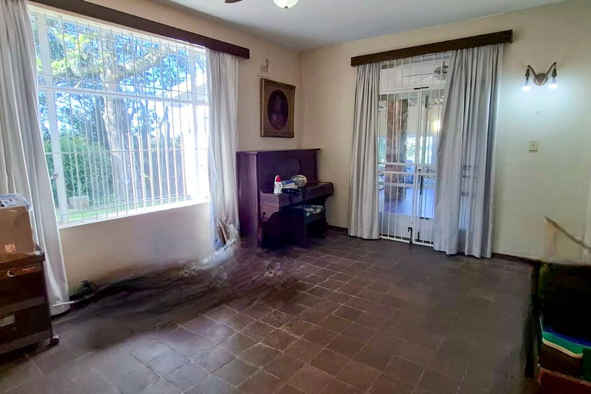 A living room featuring tiled flooring, security bars on windows, and an arched entryway, offering a functional space with potential for modernization.