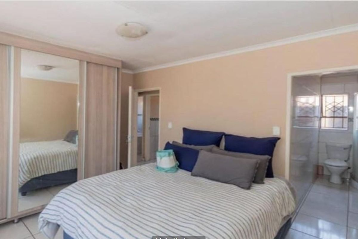 Spacious bedroom featuring built-in mirrored sliding wardrobes and an attached en-suite bathroom with a shower and tiled finishes.