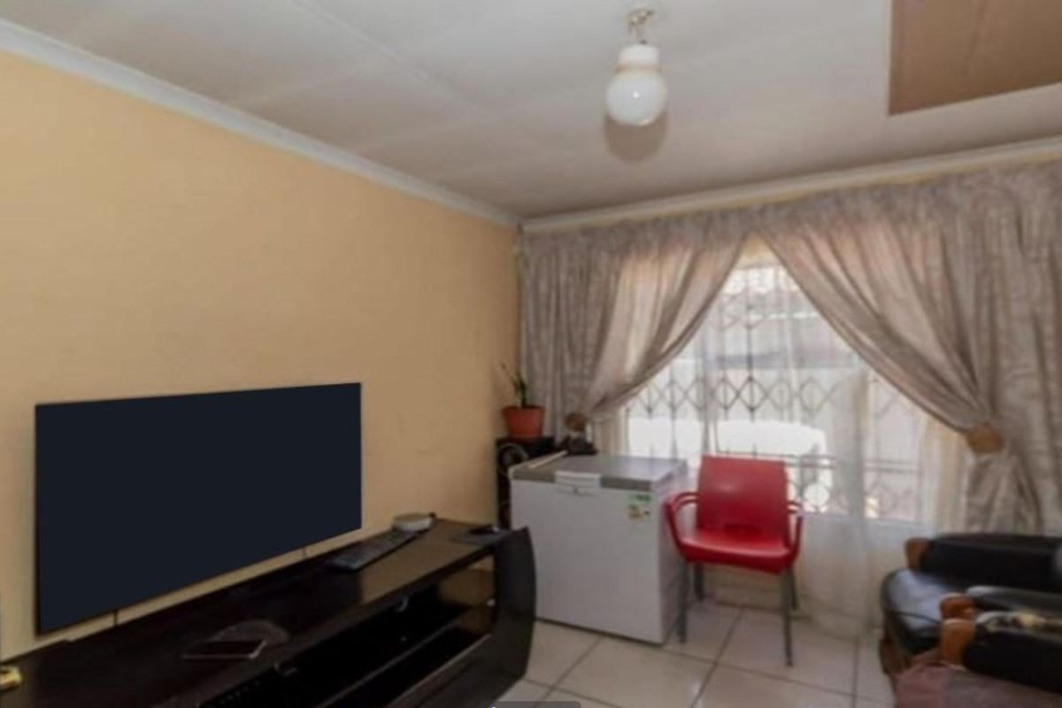 A living room area featuring tiled flooring and a security gate over the window, providing a functional space with potential for cosmetic updates.