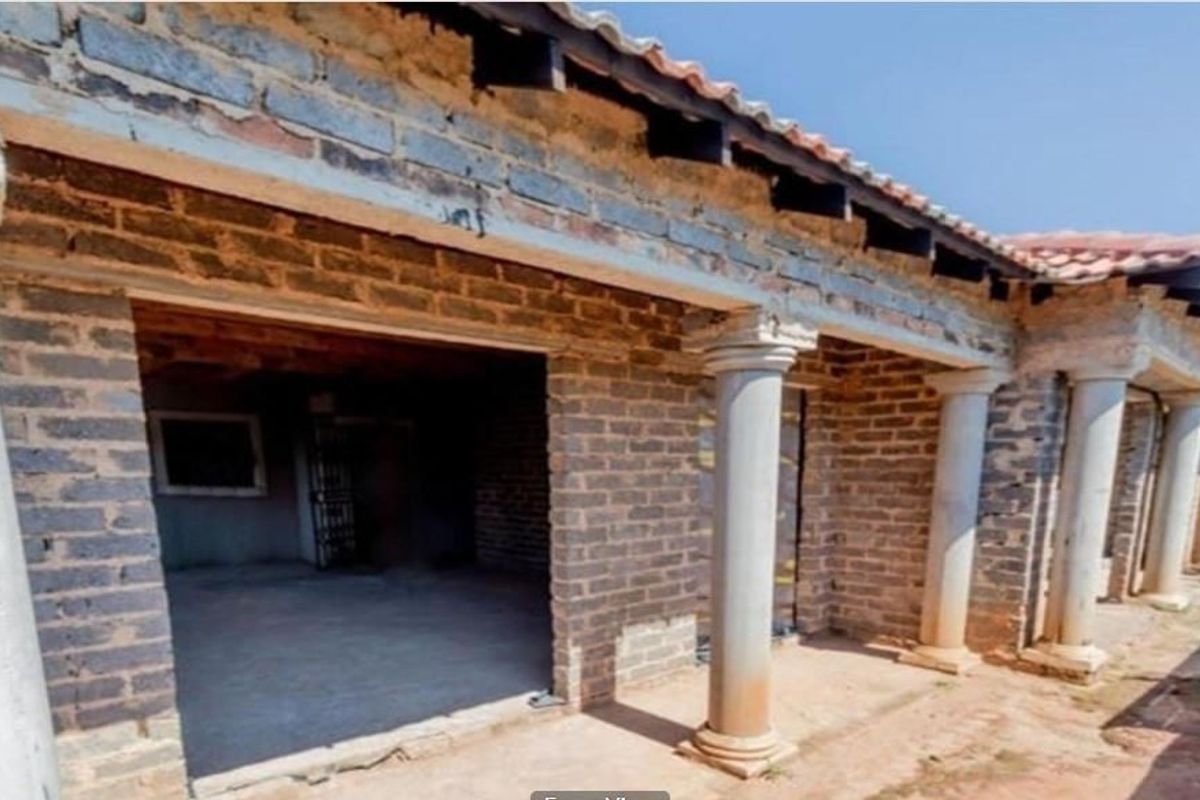 An unfinished rear exterior view featuring exposed brickwork, concrete columns, and a tiled roof structure, presenting a significant renovation opportunity.