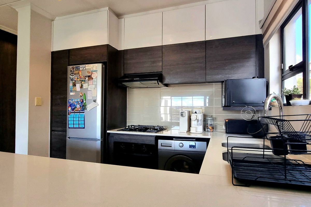 Modern kitchen featuring two-tone cabinetry, stone countertops, integrated gas hob, extractor fan, and built-in oven with a sleek tiled backsplash.