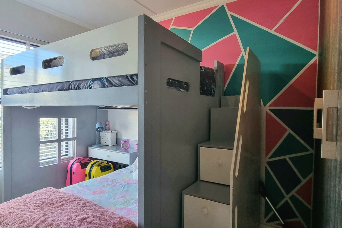 A bedroom featuring a large window with fitted blinds and a built-in wardrobe, showcasing a vibrant geometric accent wall.