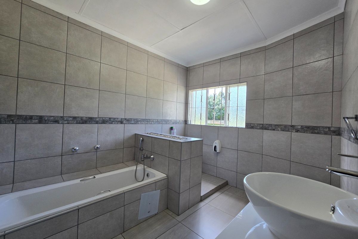 A modern, spacious bathroom featuring large-format grey wall tiles, a built-in bathtub, and a contemporary vessel sink.