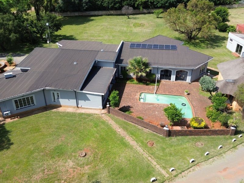 Aerial view of a farm property featuring a main residence with a metal roof, solar panels, a swimming pool, and a separate thatched structure.