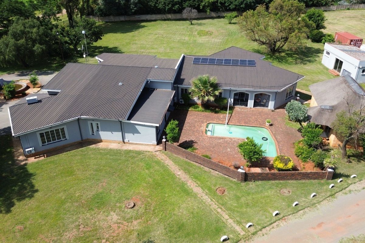 Aerial view of a farm property featuring a main residence with a metal roof, solar panels, a swimming pool, and a separate thatched structure.
