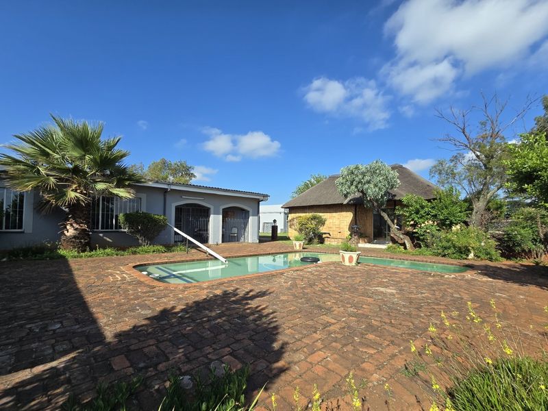 Outdoor pool area featuring a brick-paved patio, swimming pool, and a traditional thatched-roof building in a farm setting.
