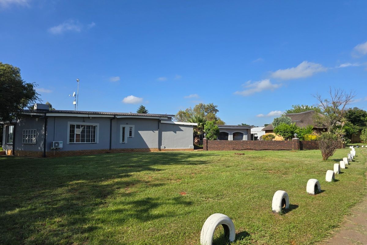 A view of the rear exterior of the farm property, featuring a large lawn, brick boundary wall, and single-story building structure.