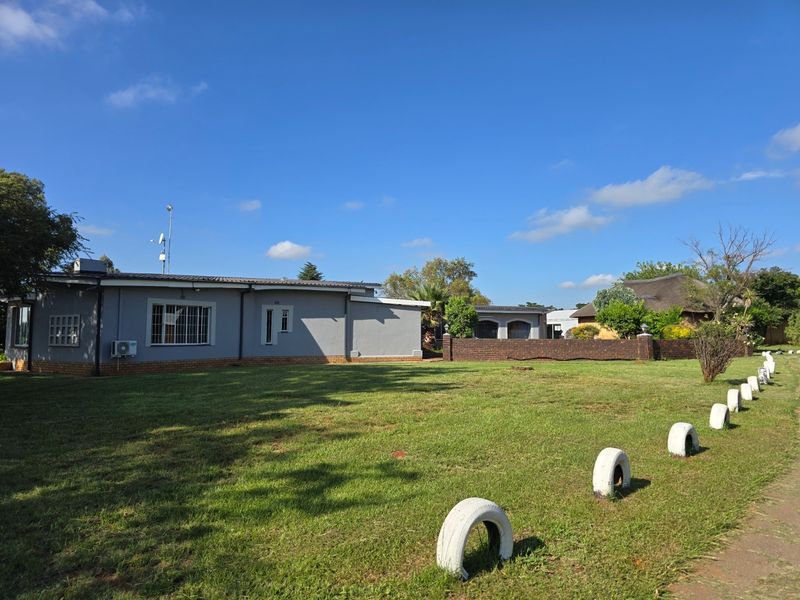A view of the rear exterior of the farm property, featuring a large lawn, brick boundary wall, and single-story building structure.