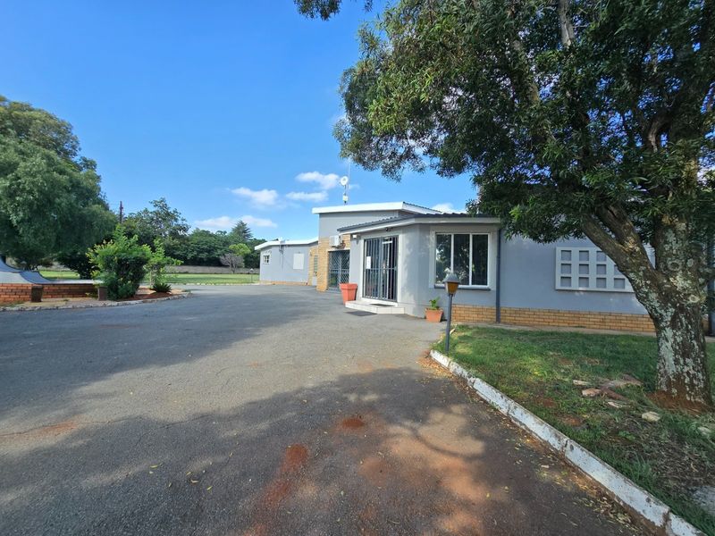Front exterior view of the farm property featuring an asphalt driveway, brick-based building structure, and security installations.