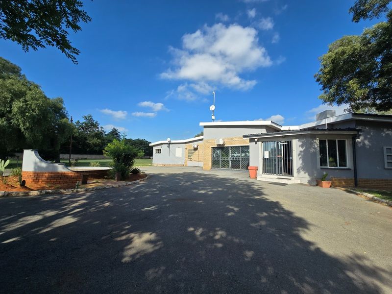 Front view of the farm property featuring an expansive asphalt driveway, brick retaining wall, and secure building entrance with security gates.