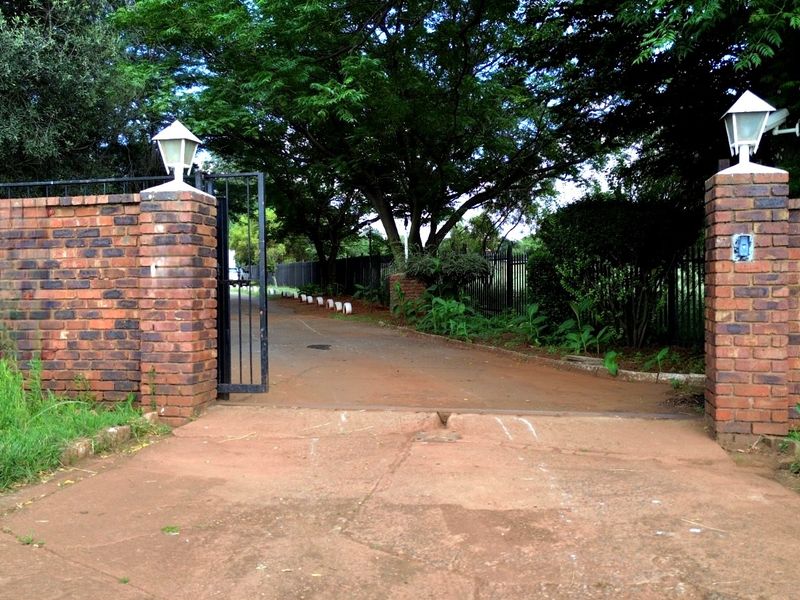 Entrance to the property featuring brick pillars, security gate, and a paved driveway leading into the grounds.