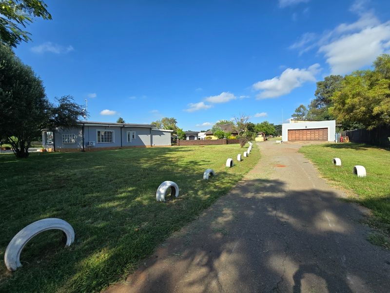 Wide-angle view of the property exterior featuring a large lawn, asphalt driveway, and a detached garage building under a clear blue sky.